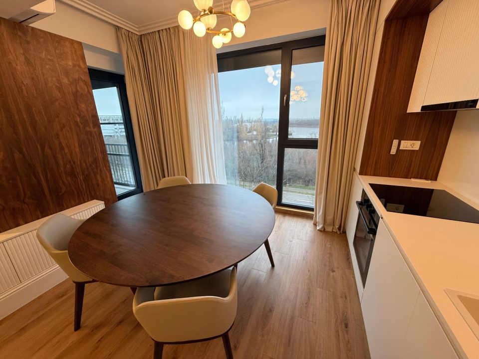 Zona de dining, cu masă rotundă de nuc și vedere spre lac